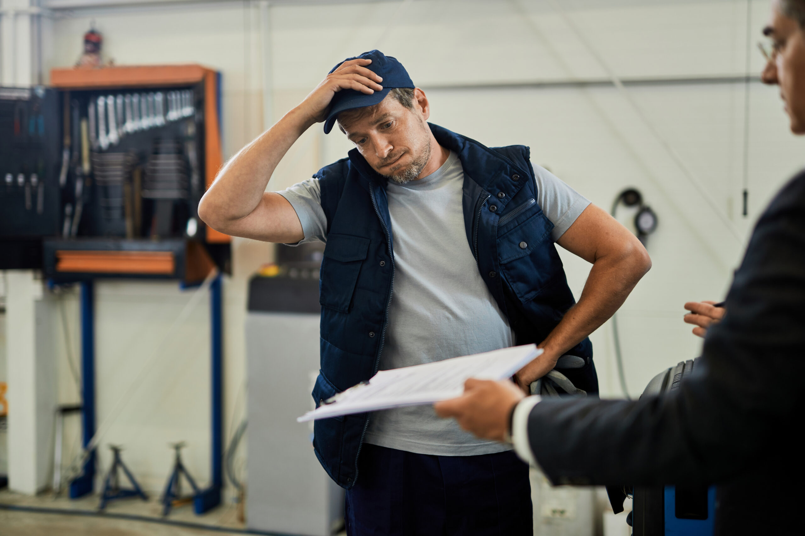 Distraught car mechanic going through problematic paperwork with his manager in auto repair shop.