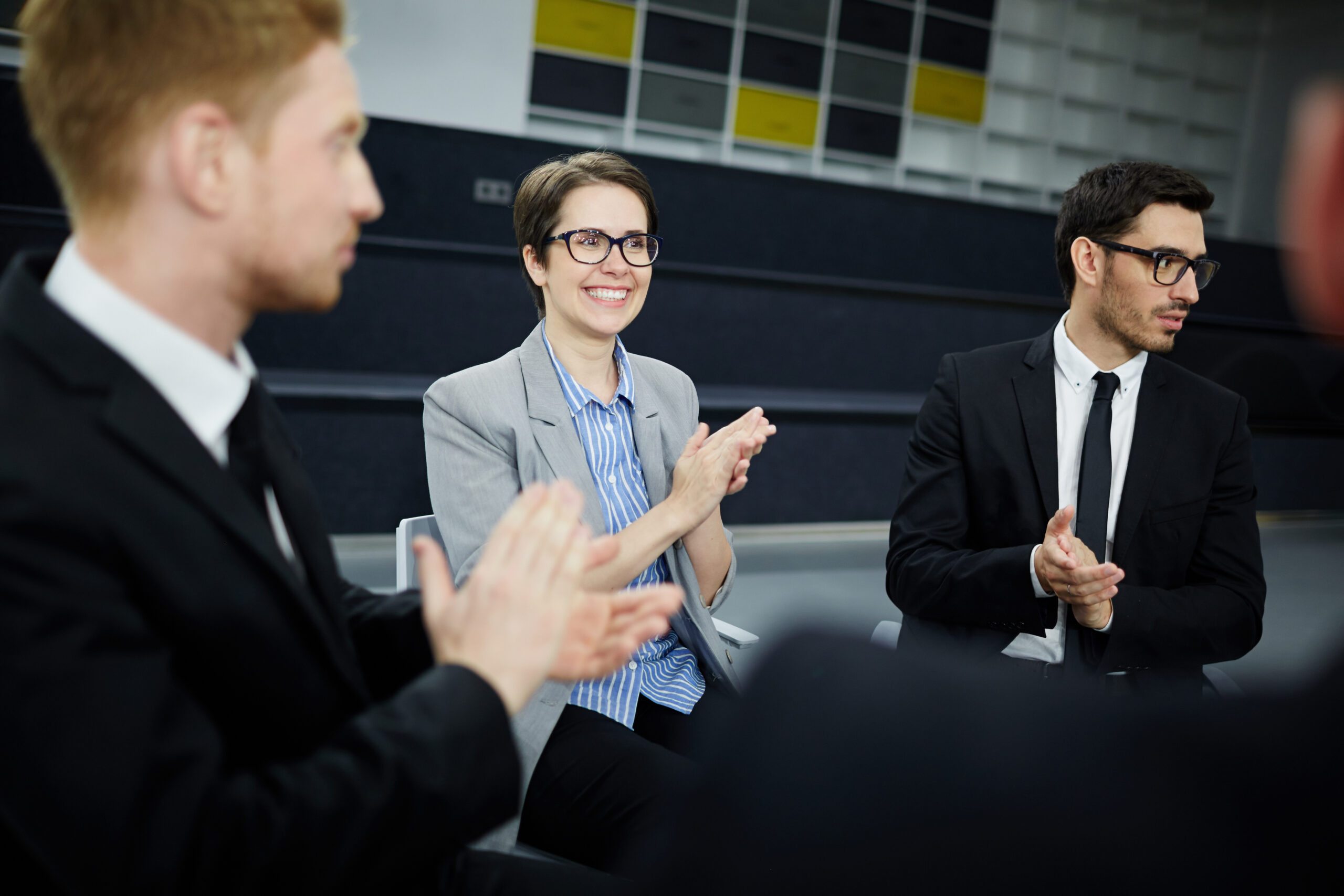 Happy businesswoman and her colleagues clapping hands after report of their co-worker during start-up discussion